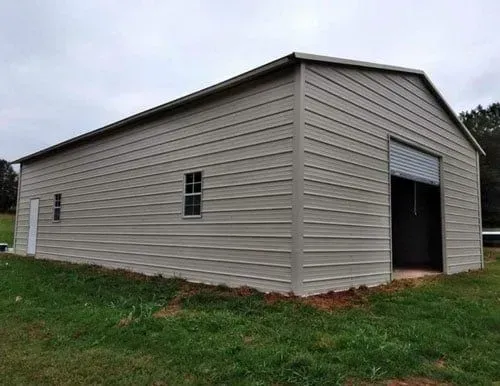 A large metal barn is sitting in the middle of a grassy field.