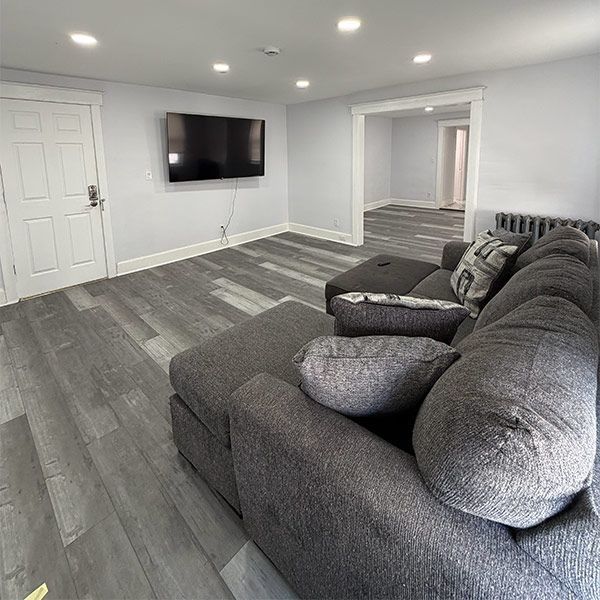 Gray sectional sofa in a bright, empty living room with wall-mounted TV and gray wood flooring