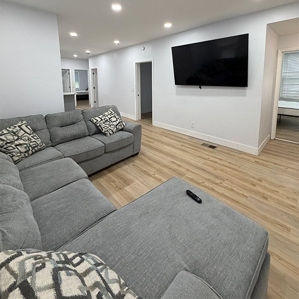 Modern living room with gray sectional sofa, wall-mounted TV, and light wood flooring.