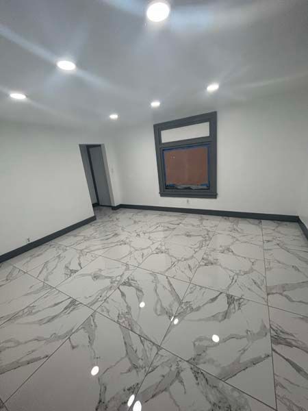 Empty modern room with white marble-pattern tile, recessed ceiling lights, gray walls, and a window
