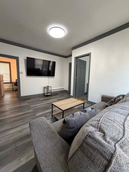 Modern living room with gray sofa, wall-mounted TV, coffee table, and gray wood floors