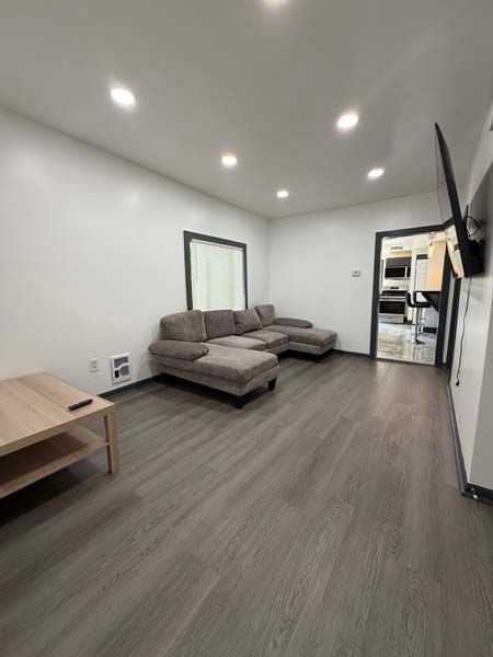 Minimal living room with gray sectional sofa, wood floor, recessed lights, and TV mounted on the wall.