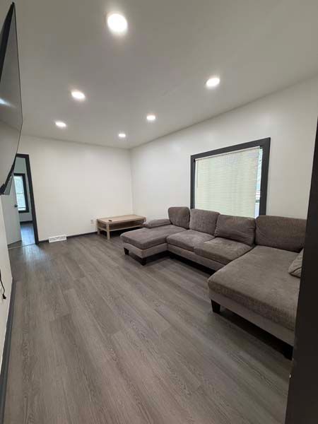 Modern empty living room with gray sectional sofa, recessed ceiling lights, and wood-look flooring