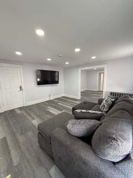Gray living room with sectional sofa, wall-mounted TV, recessed lights, and open doorway to another room
