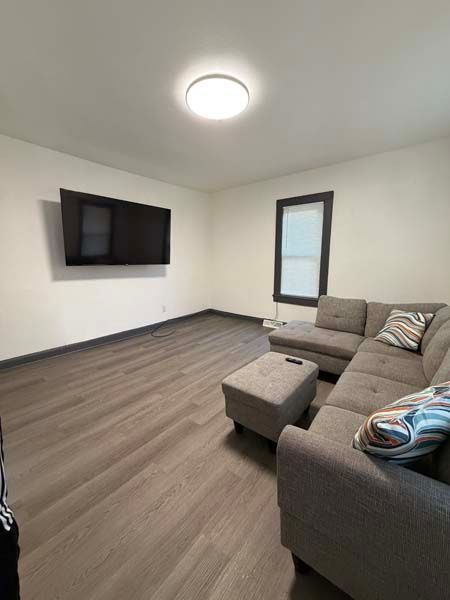 Empty living room with gray sectional, wall-mounted TV, and a bright ceiling light