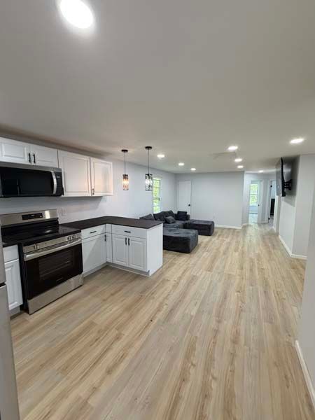 Bright open-plan kitchen and living room with white cabinets, wood floors, and gray sectional sofa.