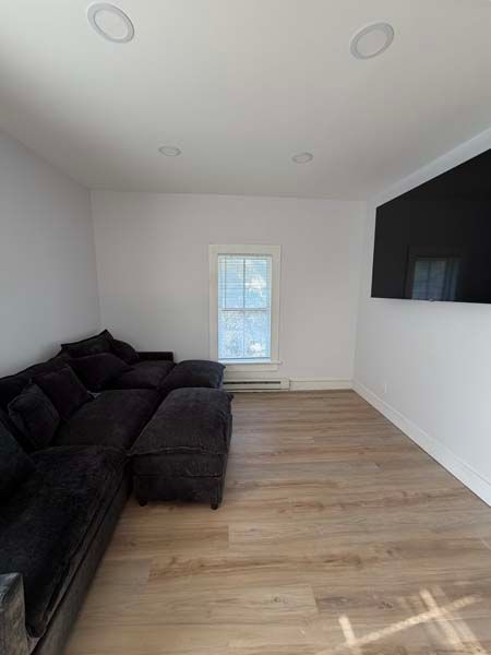 Minimalist living room with black sectional sofa, light wood floor, and wall-mounted TV.