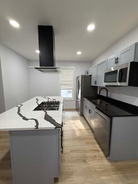 Modern galley kitchen with gray cabinets, white island, black countertops, and stainless appliances.