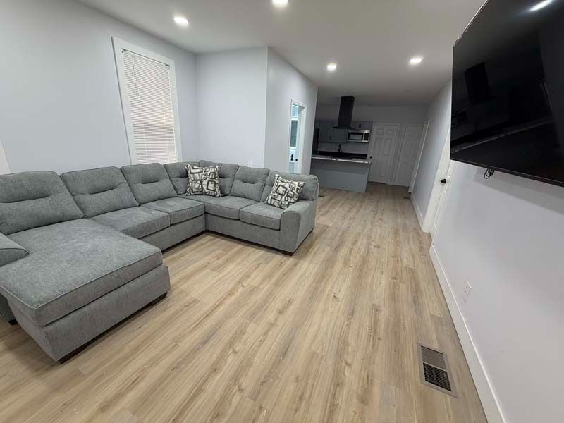 Modern gray sectional sofa in a bright living room with wood flooring and a wall-mounted TV.