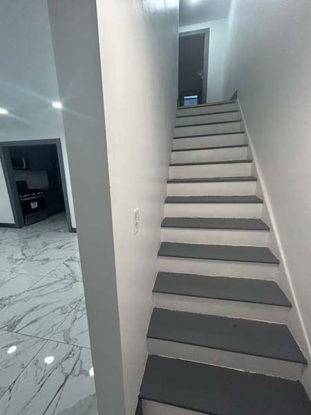 Narrow indoor staircase with light gray steps and white walls beside a tiled hallway.