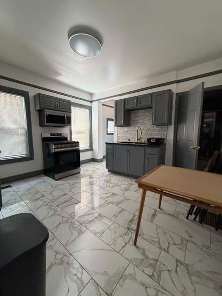 Small kitchen with gray cabinets, white marble-pattern floor, stove, microwave, and a wooden table.