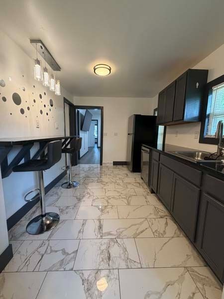 Modern kitchen with white marble floor, dark cabinets, bar stools, and black appliances