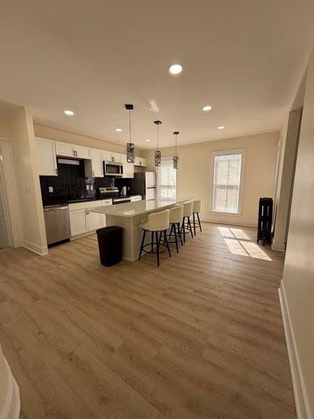 Bright kitchen with white cabinets, black island stools, and wood floors in a spacious open room