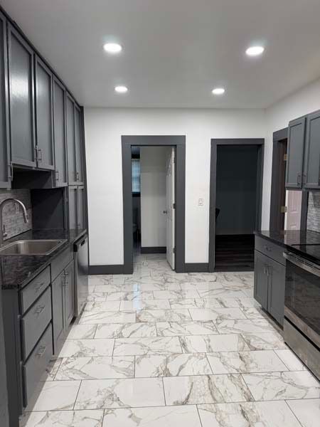 Modern gray kitchen with marble-look floor, dark cabinets, and recessed ceiling lights.