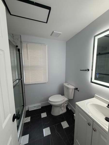 Small modern bathroom with toilet, vanity sink, black tile floor, window blinds, and glass shower door