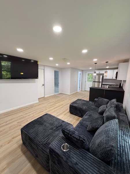 Modern open-plan living room with dark sectional sofa, light wood floors, recessed lights, and kitchen island