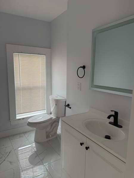 Small bathroom with toilet, vanity sink, mirror, and window with blinds
