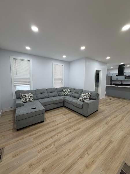Modern living room with gray sectional sofa, wood floors, recessed lights, and open kitchen area