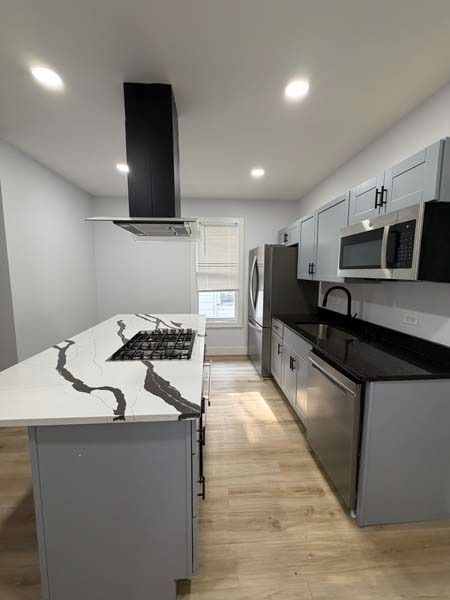 Modern galley kitchen with gray cabinets, marble island, black countertops, and stainless steel appliances