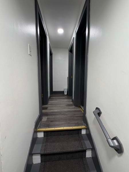 Narrow indoor staircase leading to a hallway with dark doors and white walls, viewed upward from below