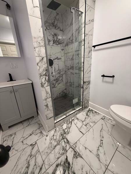 Modern bathroom with marble tile, glass shower, vanity cabinet, and white toilet