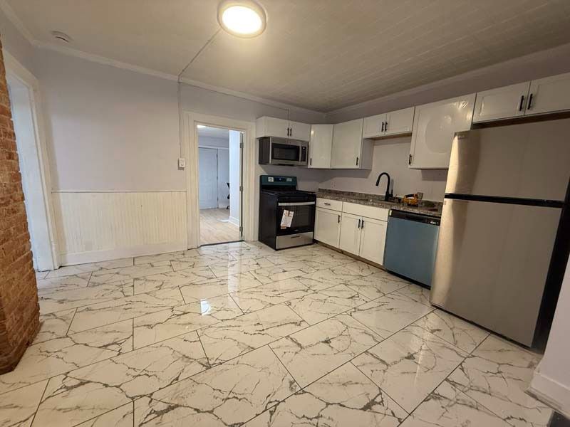 Modern kitchen with white cabinets, marble-pattern tile floor, stainless steel appliances, and a ceiling light