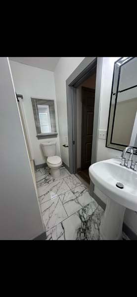 Narrow modern bathroom with toilet, sink, shower, and marble-pattern tile floor