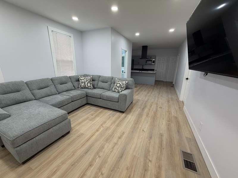 Bright living room with gray sectional sofa, wood floors, recessed lights, and wall-mounted TV.