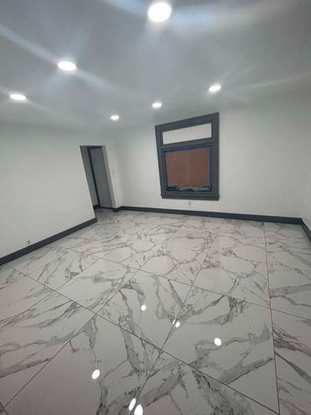Empty modern room with white marble floor, recessed lights, gray walls, and a window.
