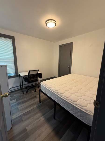 Small bedroom with a bed, desk, chair, and window with blinds.