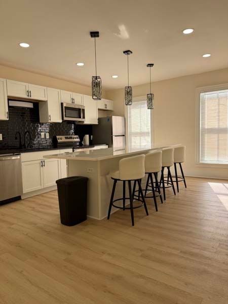 Bright kitchen with white cabinets, black island stools, and light wood floors.