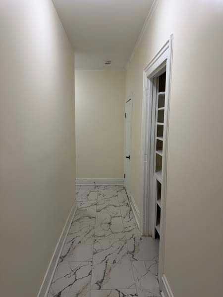 Narrow hallway with white walls, marble-pattern tile floor, and a partially open doorway on the right.