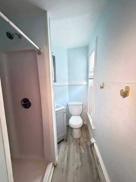 Narrow bathroom with toilet, shower stall, and light wood floor in soft pastel tones