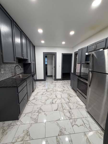 Modern kitchen with dark cabinets, stainless steel appliances, and white marble-patterned floor tiles.