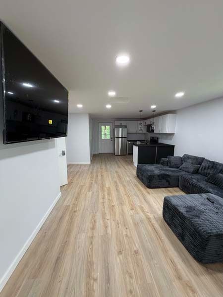 Modern living room with black sectional sofa, wood floors, wall-mounted TV, and open kitchen area