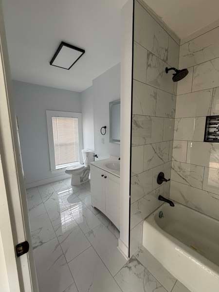 Modern white bathroom with tiled floors, vanity, toilet, and tub/shower area viewed from the doorway