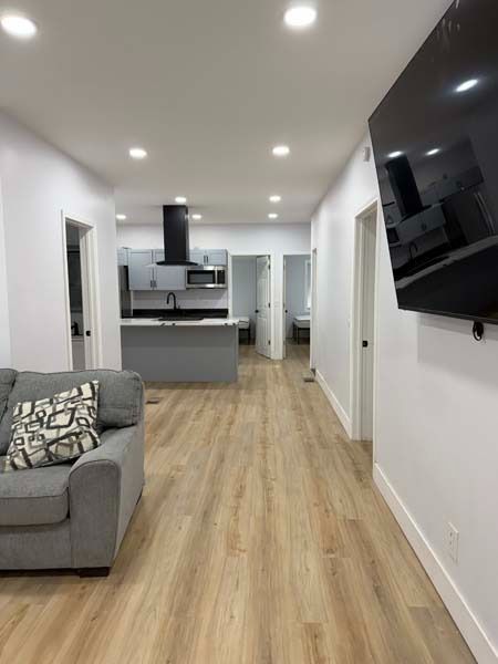 Modern open-plan living room with gray sofa, wall-mounted TV, and kitchen in the background