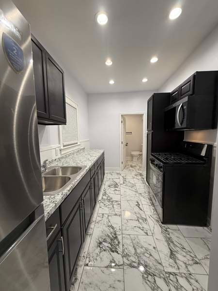 Modern kitchen with dark cabinets, marble floor, stainless sink, and bright recessed ceiling lights