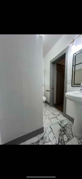Bathroom hallway with marble floor, white walls, and a sink visible on the right