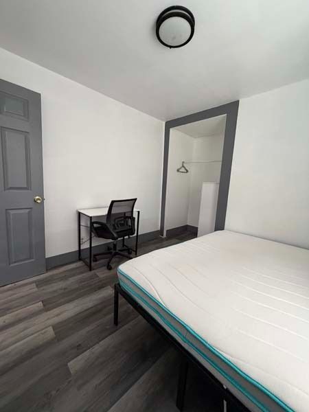 Small bedroom with a bed, desk, chair, closet mirror, and gray walls.