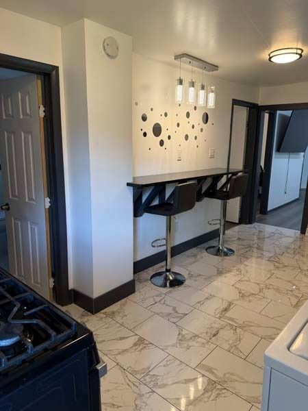 Modern kitchen with marble floor, bar stools, stove, and patterned wall decor