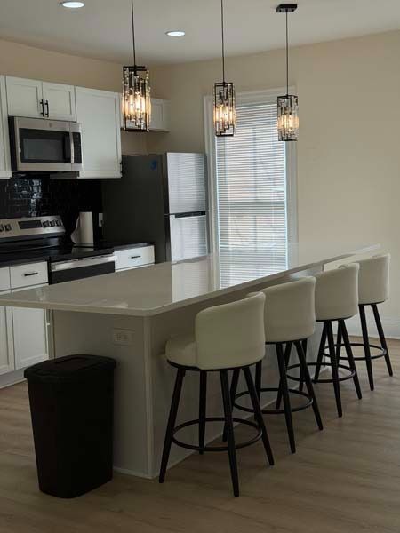Modern kitchen with white island, four stools, stainless appliances, and hanging pendant lights