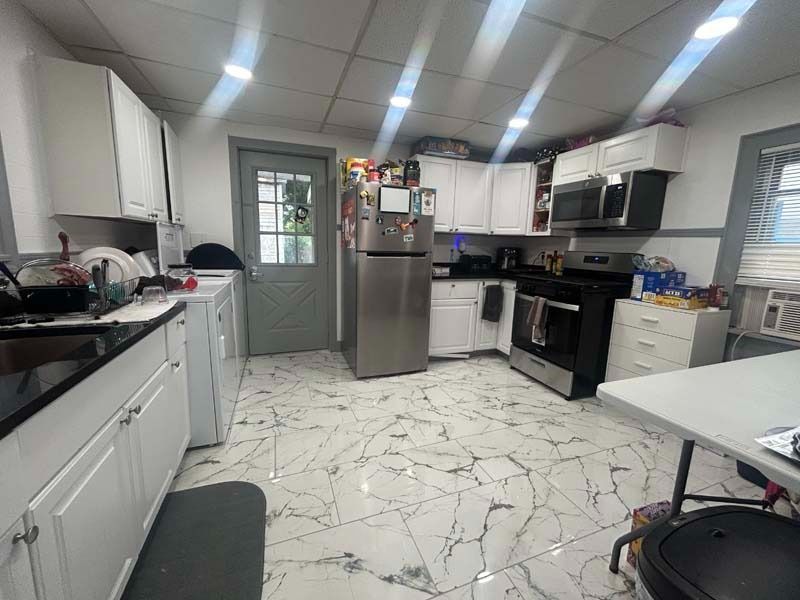 Bright modern kitchen with white cabinets, stainless steel appliances, and marble-patterned tile floor