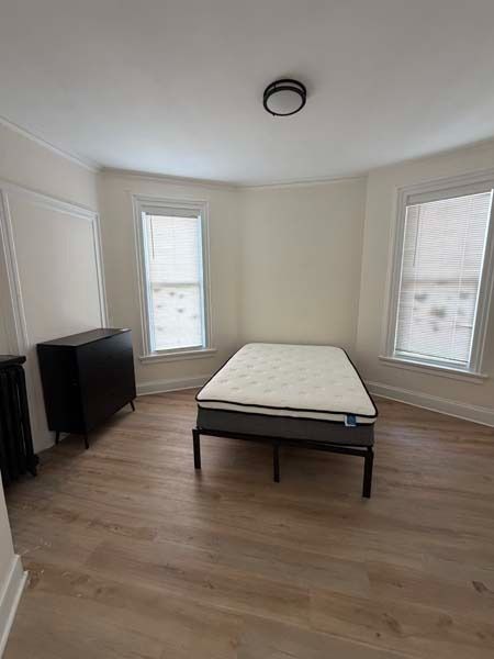 Sparse bedroom with a bed, two windows, and a small TV on a wood floor