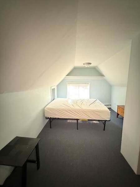 Small attic bedroom with a bed, black bench, and window at the far end.