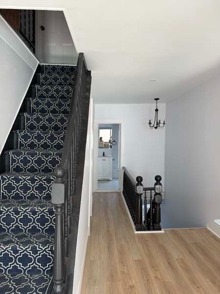 Hallway with patterned staircase, light wood floor, white walls, and a small chandelier.