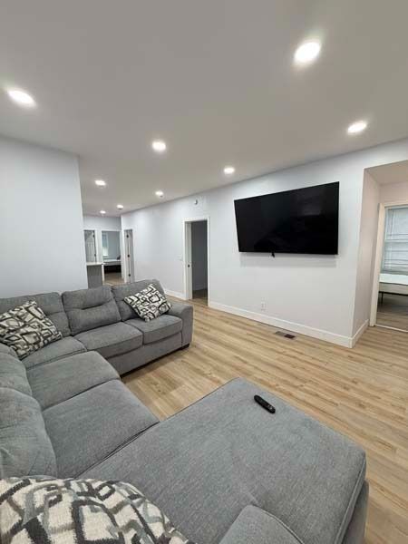 Bright modern living room with gray sectional sofa, wall-mounted TV, and recessed ceiling lights