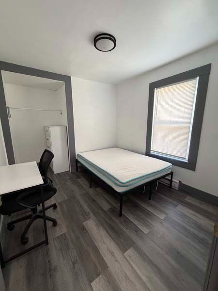 Small furnished room with a bed, desk, chair, and window on the right