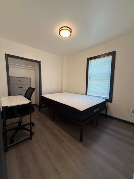 Small bedroom with a bed, desk chair, dresser, and two windows with blinds
