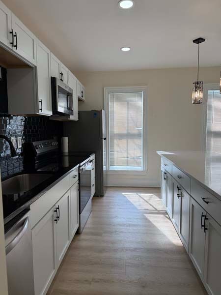 Bright modern kitchen with white cabinets, black countertops, and a narrow island walkway.